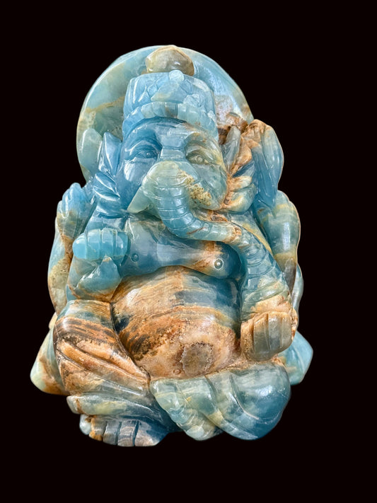 Blue onyx Ganesha crystal carving front view on dark table showing sky blue and caramel banding