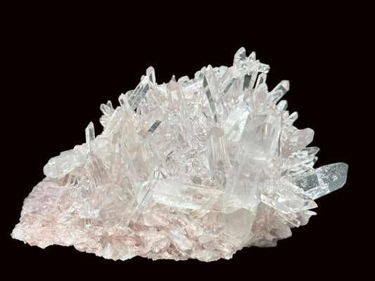 A cluster of pink Lemurian quartz crystals on a black surface with a white furry background.